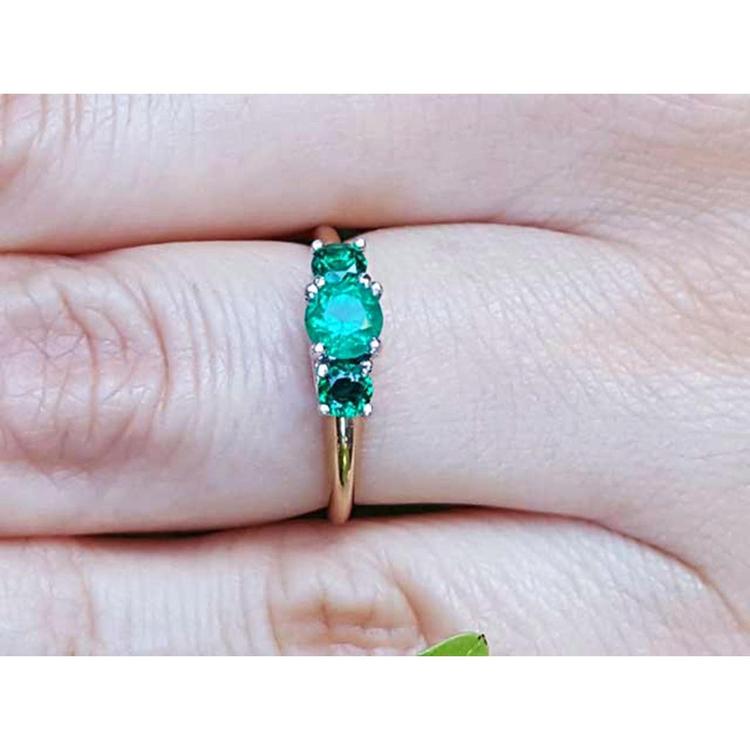 An emerald ring with round cut emeralds, Symbolizing May's birthstone, on a finger's person.
