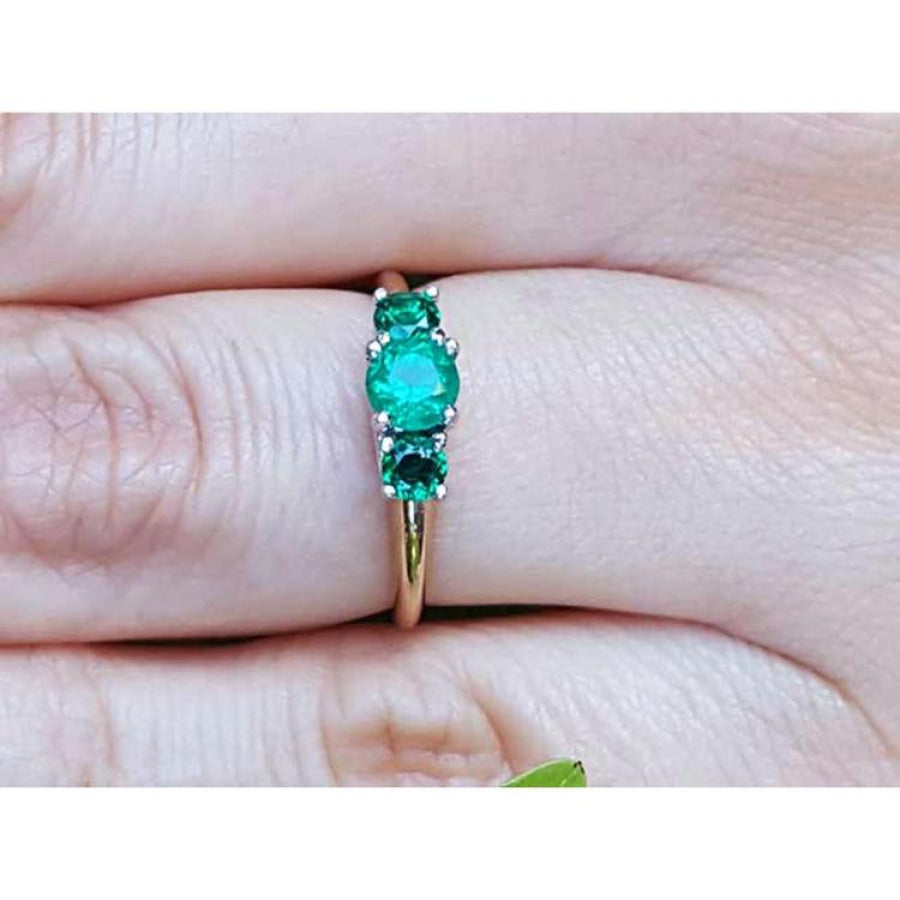 An emerald ring with round cut emeralds, Symbolizing May's birthstone, on a finger's person.