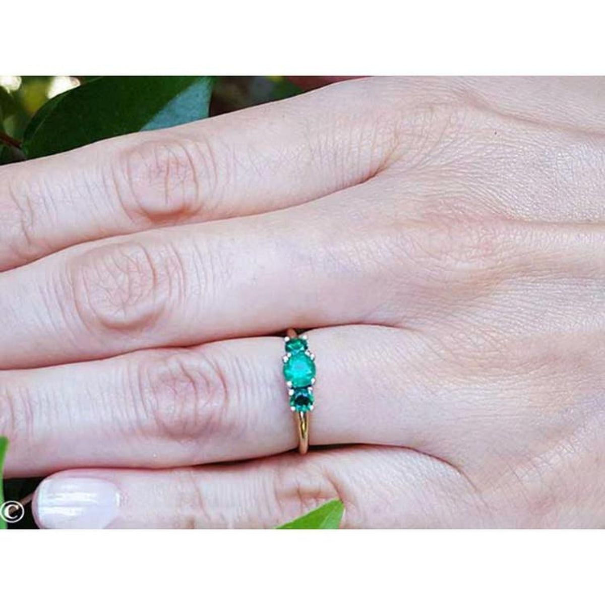 Round cut three-stone emerald ring with prong-set stones in Lucida style, crafted in white and yellow gold.