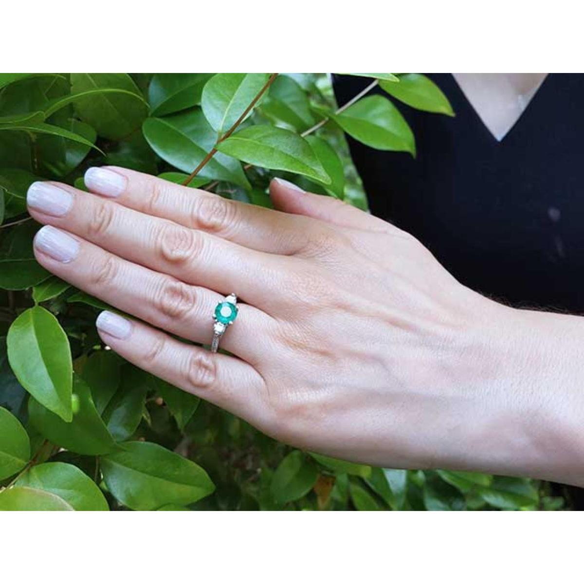 Hand wearing a real Colombian emerald ring against a green leafy background.