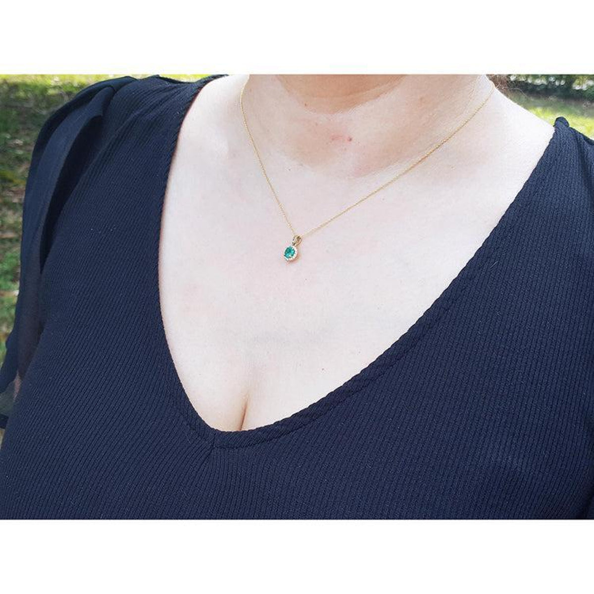 Petite round cut deep green Colombian emerald necklace with halo diamonds in 14k yellow gold on a woman's neck.