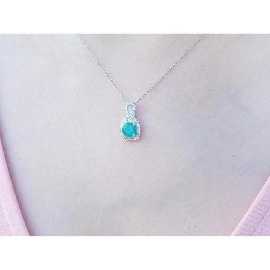 Round Colombian emerald and diamond halo pendant in 18K white gold, worn on a woman's neck.