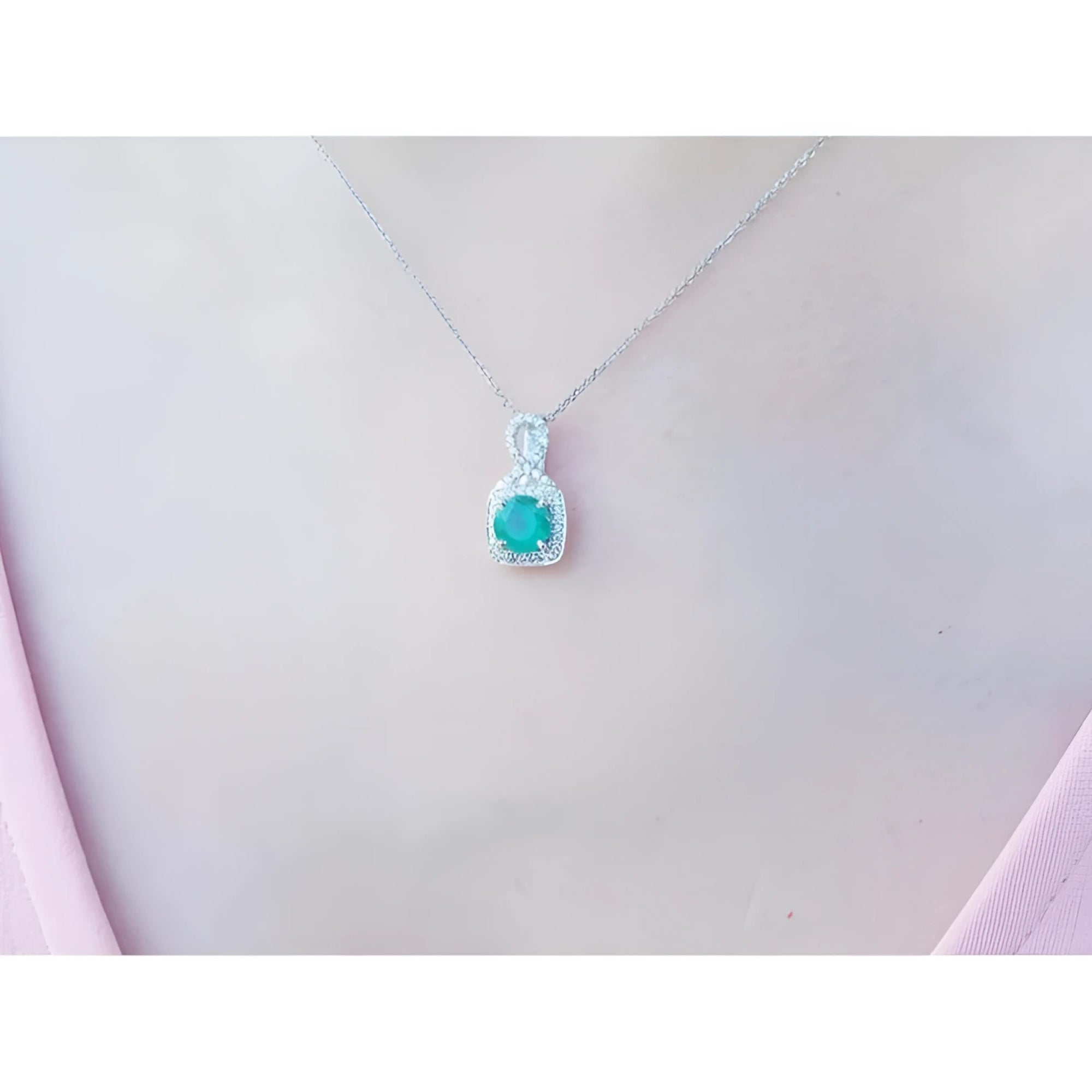 Round Colombian emerald and diamond halo pendant in 18K white gold, worn on a woman's neck.