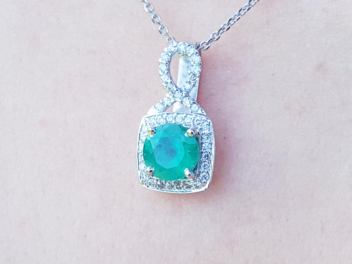A 18k white gold pendant with a natural colombian emerald on a light pink background.