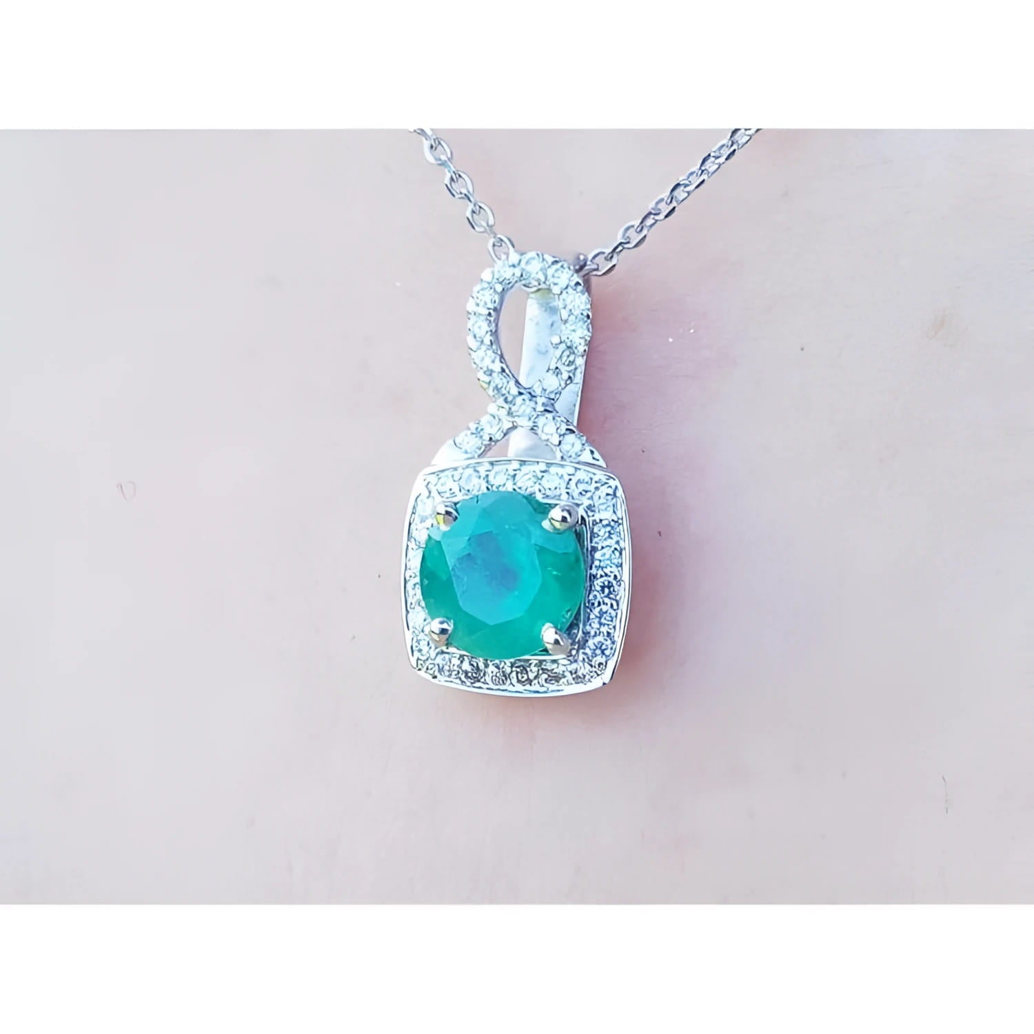 A 18k white gold pendant with a natural colombian emerald on a light pink background.