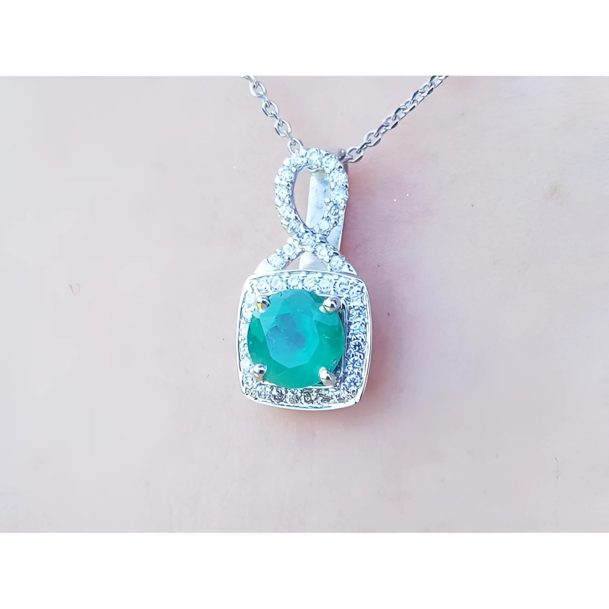 A 18k white gold pendant with a natural colombian emerald on a light pink background.