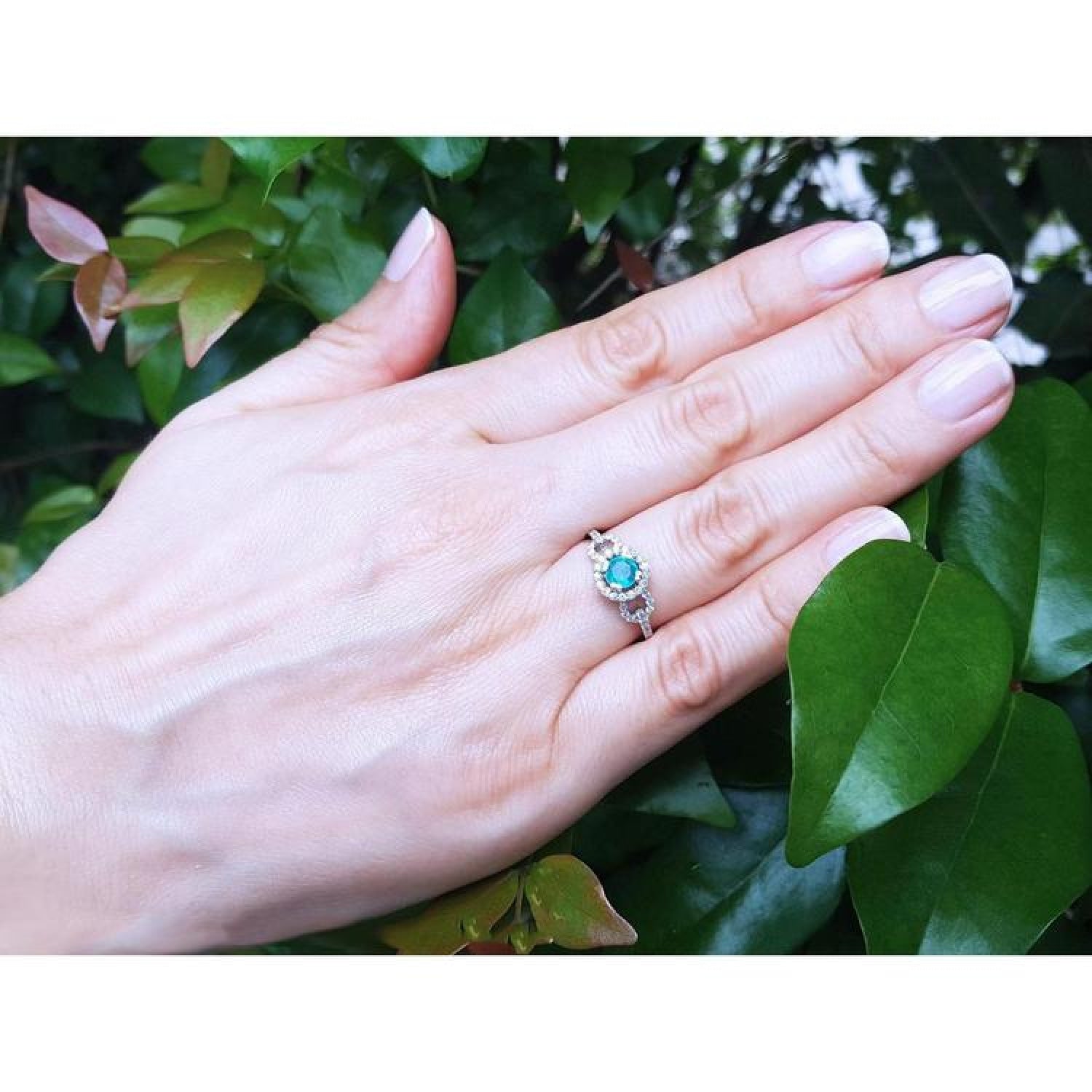 Round cut emerald halo ring with natural diamonds in 14K white gold on a woman's hand.