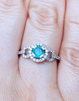 A round cut emerald surrounded by a halo diamond in white gold on a finger.