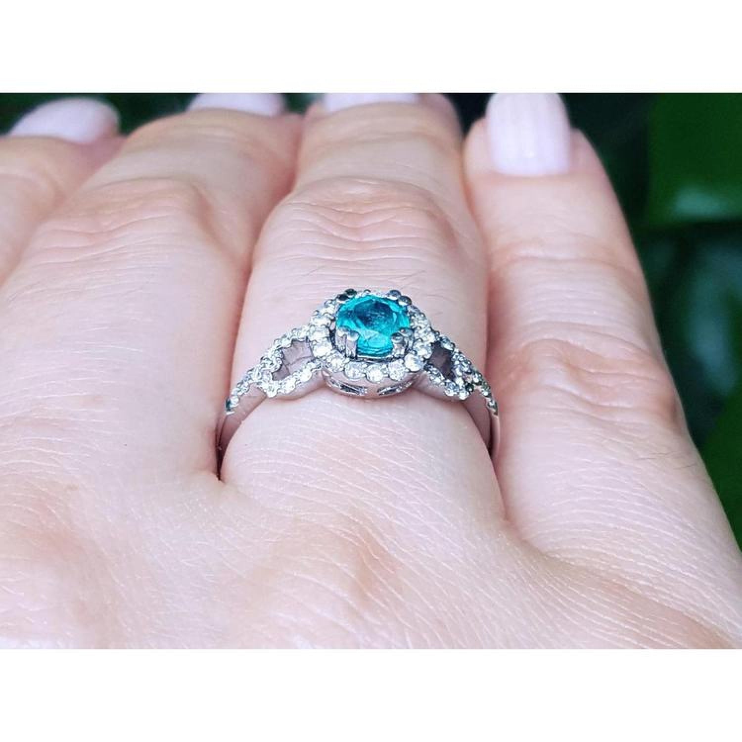 Round cut emerald halo ring with natural diamonds set in 14K white gold on a hand.