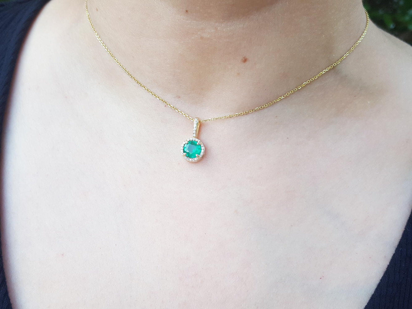 Gold necklace with a round cut natural emerald pendant necklace on a person&#39;s neck.