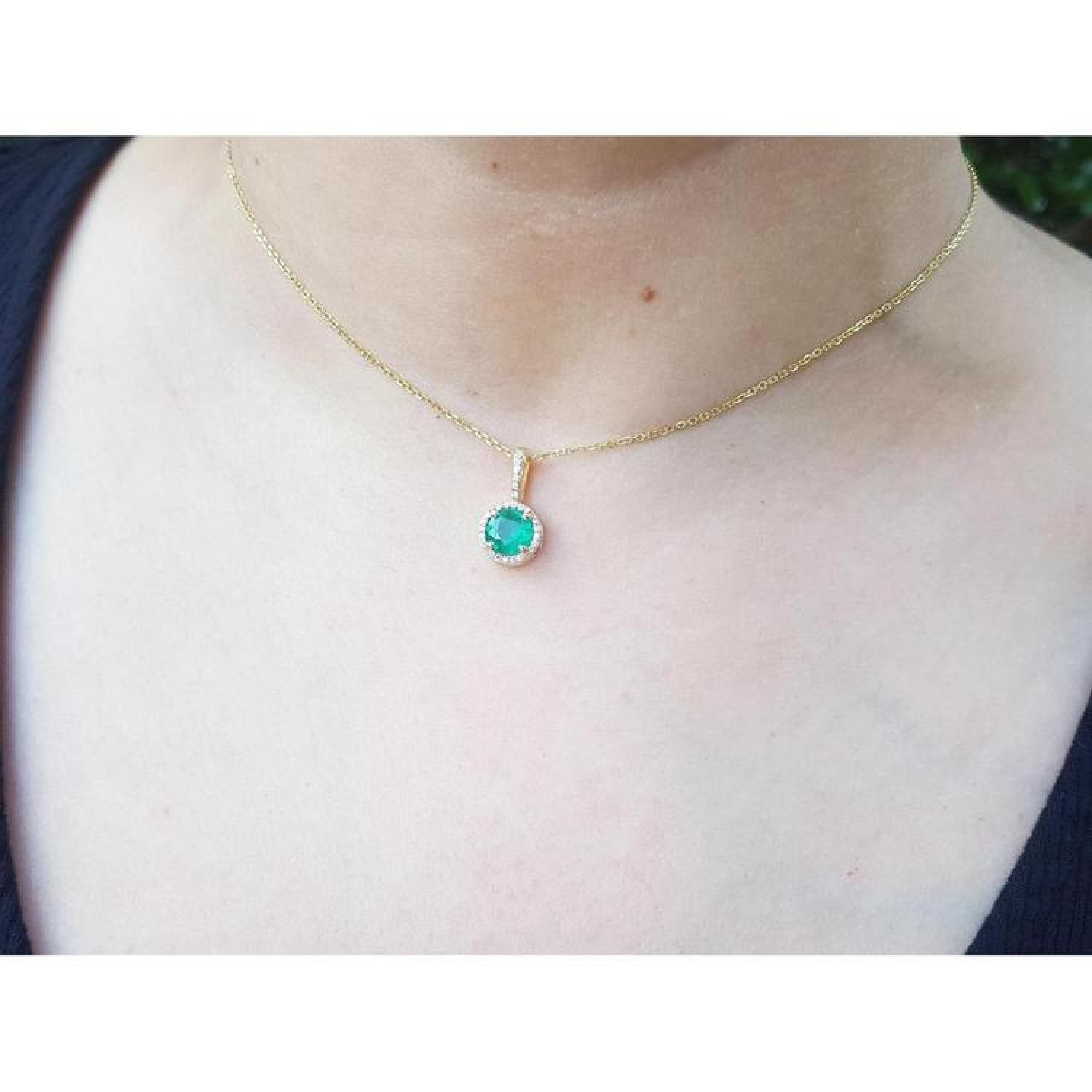 Round cut Colombian emerald pendant necklace with halo diamonds on a 14K gold chain.