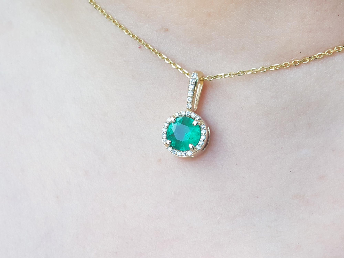 A closer view of a natural round cut emerald pendant necklace on a person&#39;s neck.