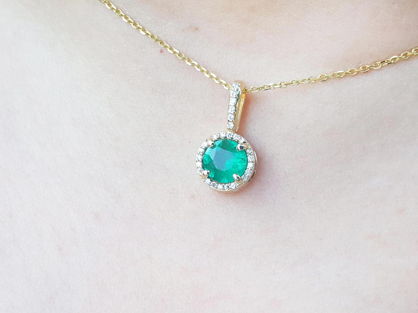 Gold necklace with a round cut natural emerald pendant on a person's neck.