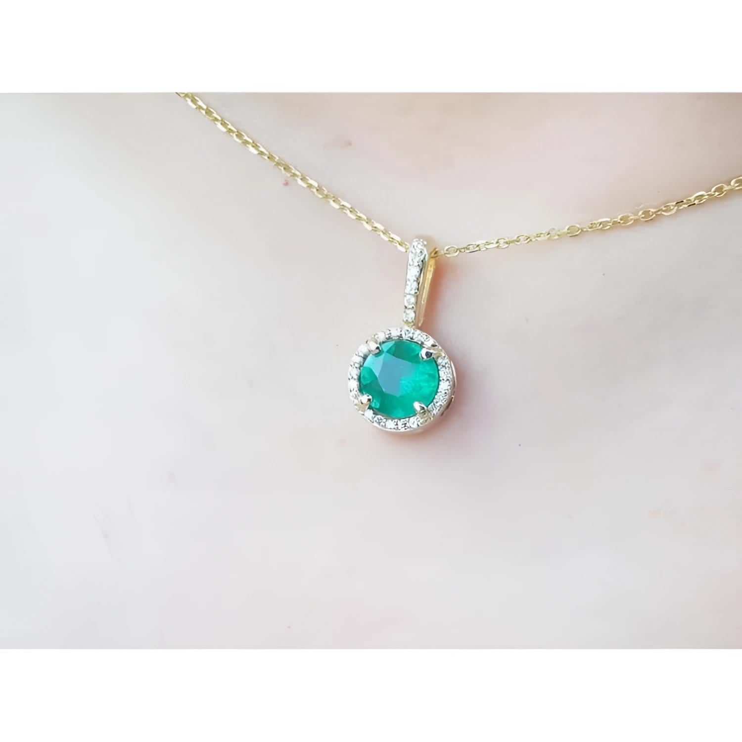 Gold necklace with a round cut natural emerald pendant on a person's neck.