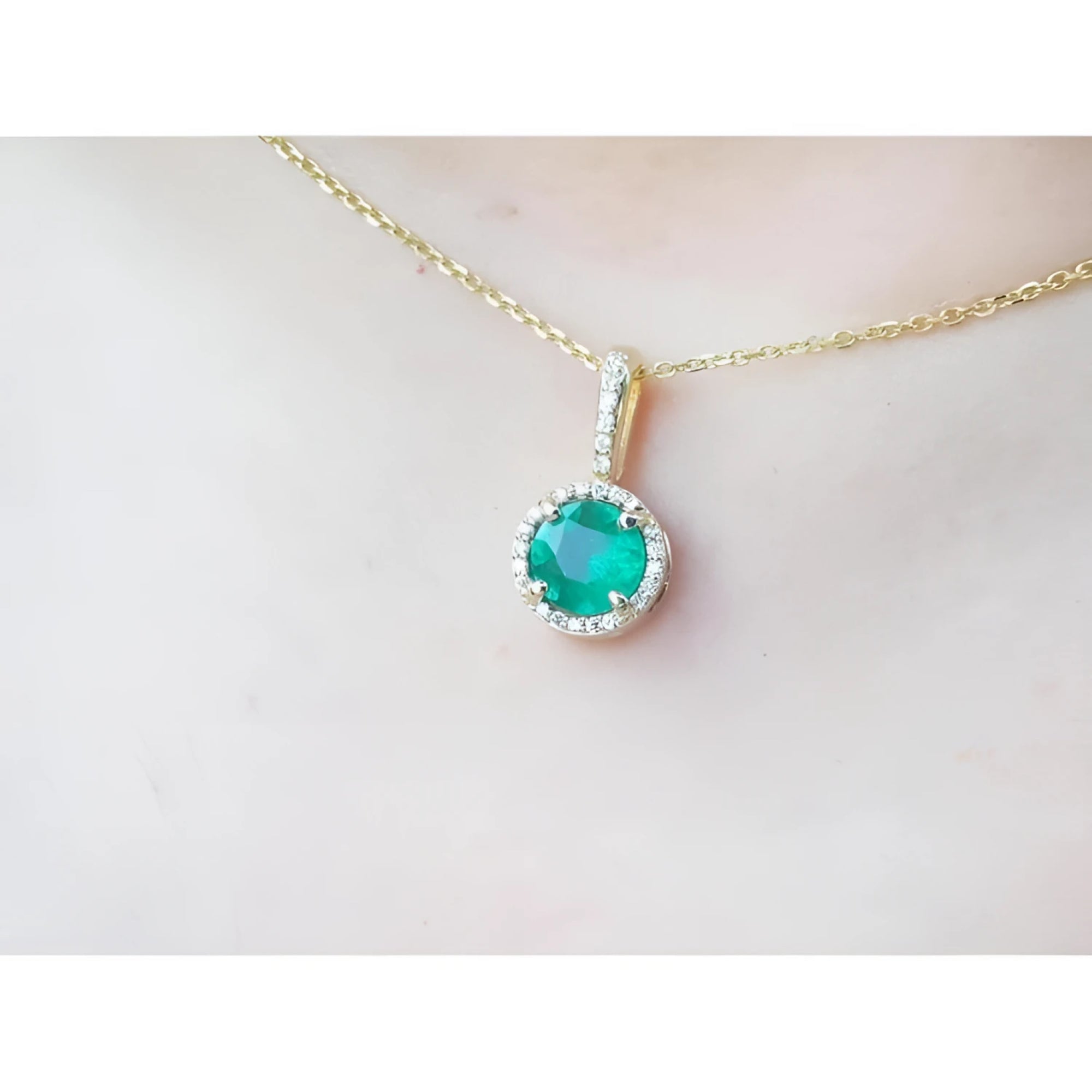Gold necklace with a round cut natural emerald pendant on a person's neck.