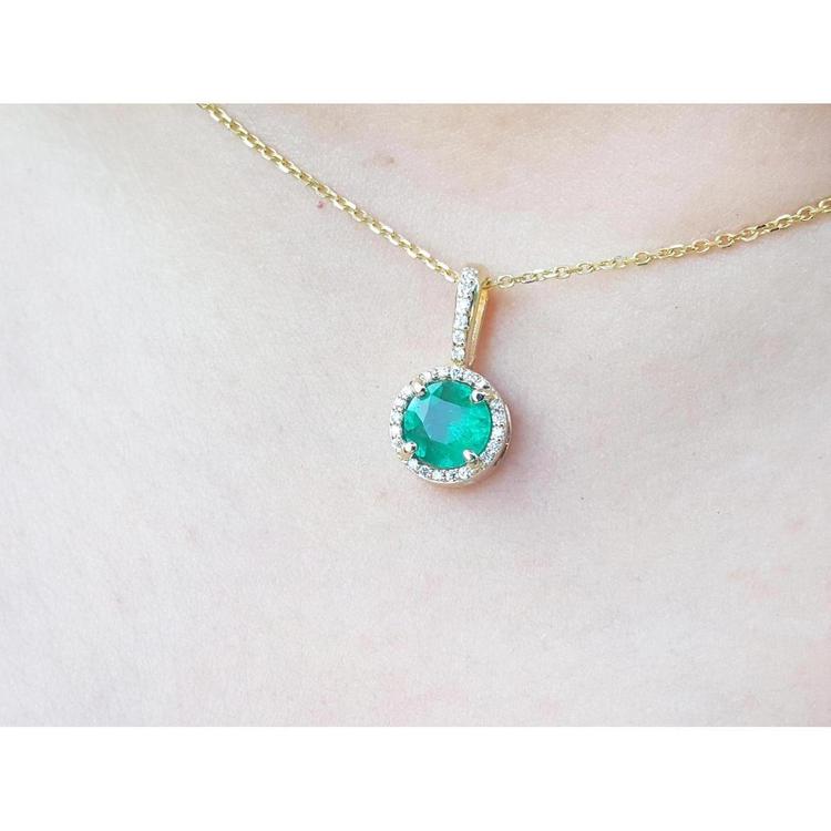 Gold necklace with a round cut natural emerald pendant on a person's neck.