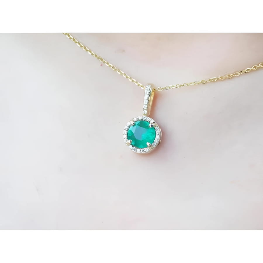 Gold necklace with a round cut natural emerald pendant on a person's neck.
