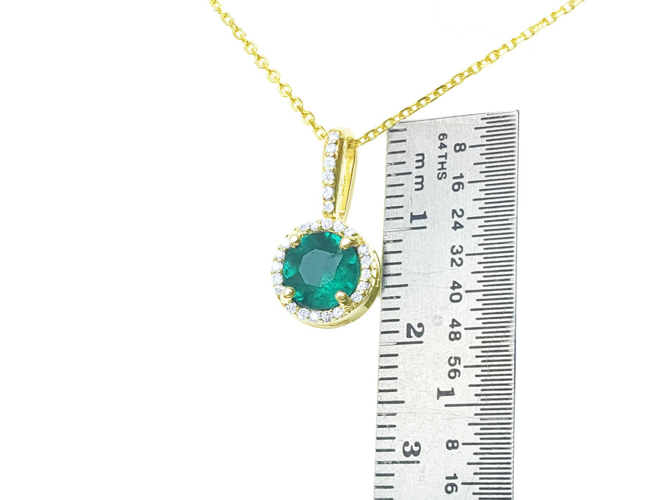 Gold pendant with a round cut colombian emerald next to a ruler on a white background.