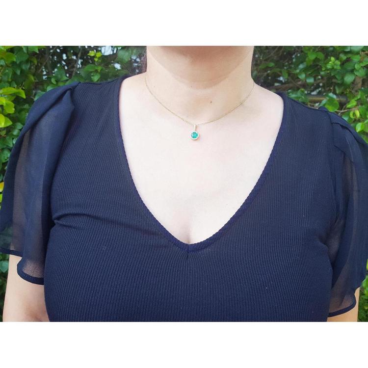 A woman wearing an emerald pendant necklace in a navy blue dress against a green leafy background.