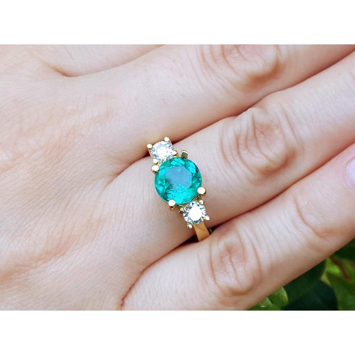 A 18k yellow gold with round cut emerald rings on a hand.