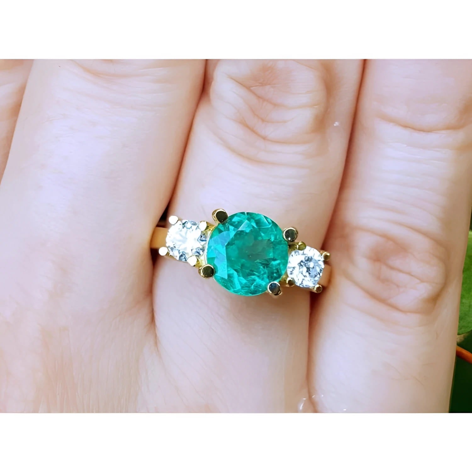 18k yellow gold GIA certified round cut colombian emerald ring with two side diamonds on a finger.