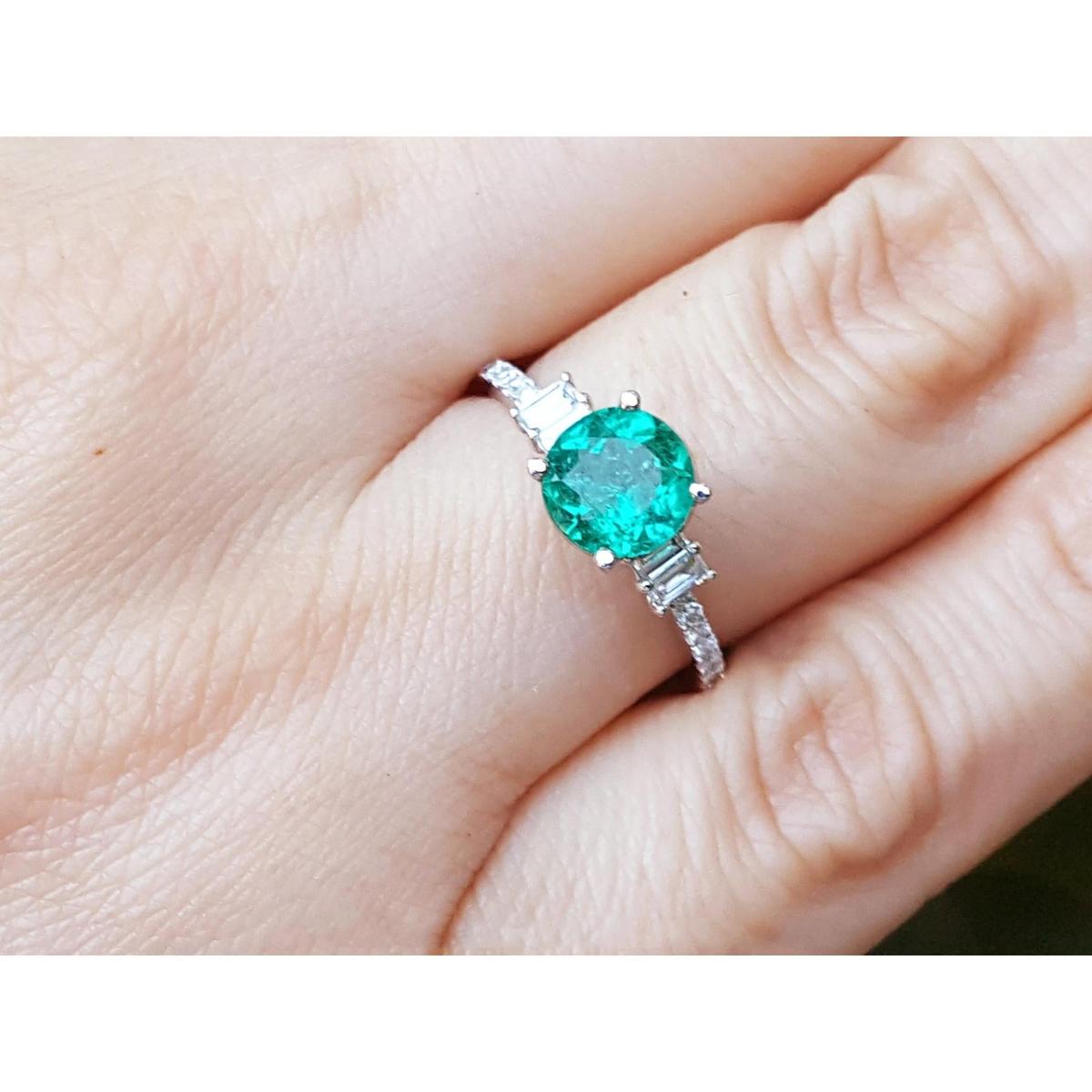 A round cut natural Colombian emerald ring on a finger.