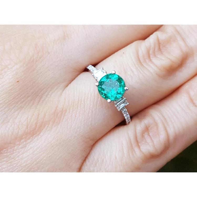 1.10 ct. round Colombian emerald ring with baguette side diamonds in 14K white gold on a hand.