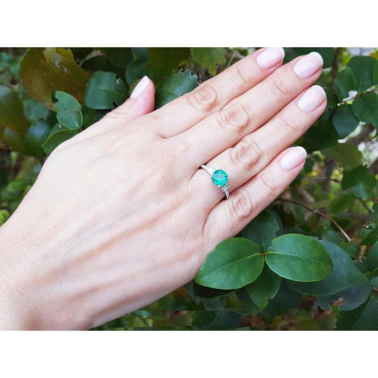 Round cut Colombian emerald ring with baguette side diamonds on a woman's hand, 14K white gold.