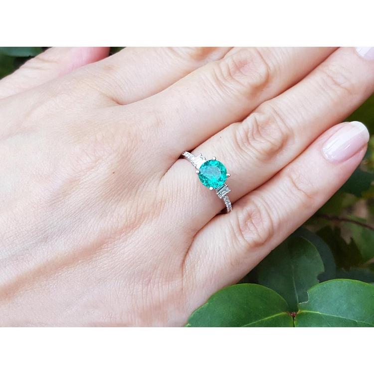 Round cut Colombian emerald ring with baguette side diamonds in 14K white gold on a hand.