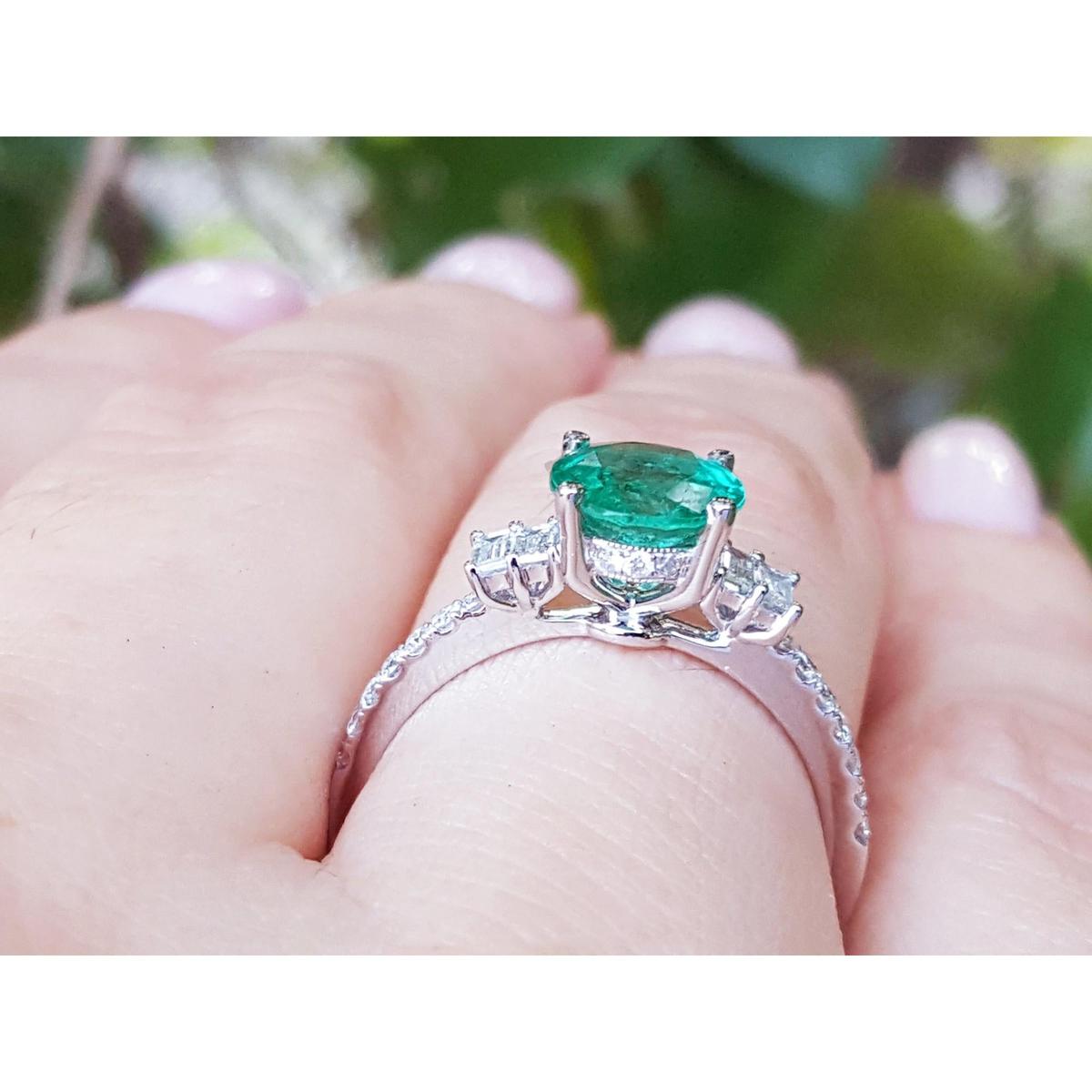Emerald ring with diamond accents on a hand against a blurred green background.