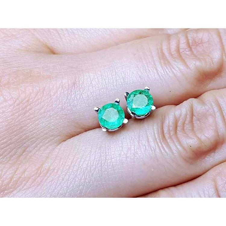 0.89 ct. round Colombian emerald stud earrings in 14k white gold, held on a hand.