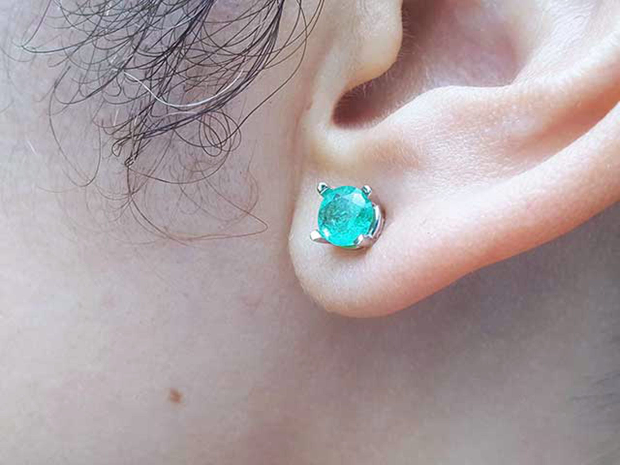 Close-up of an ear wearing a Colombian emerald stud earring.