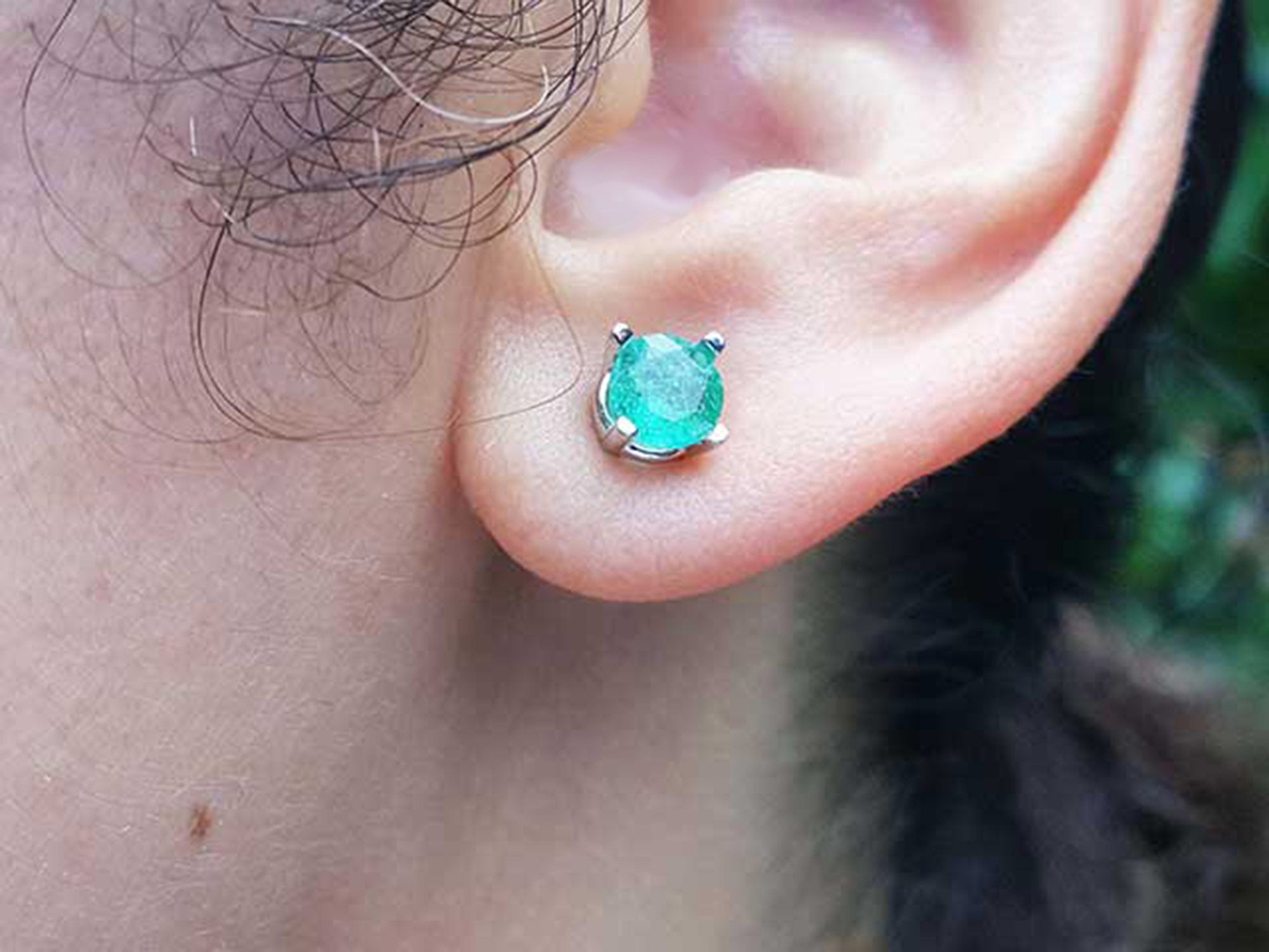 Close-up of an ear wearing a Colombian emerald stud earring with a blurred background