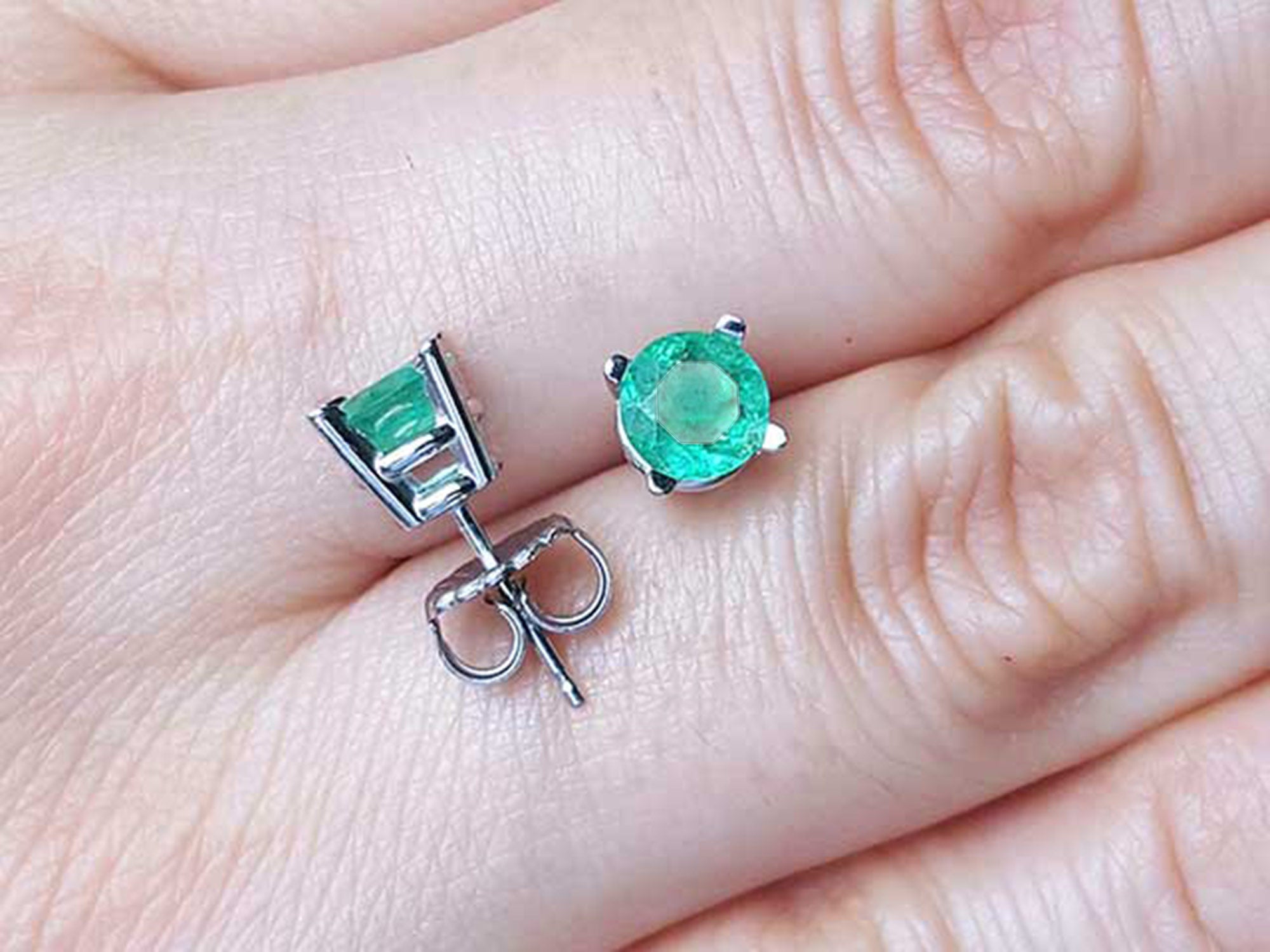 Colombian emerald stud earrings round cut on fingers.