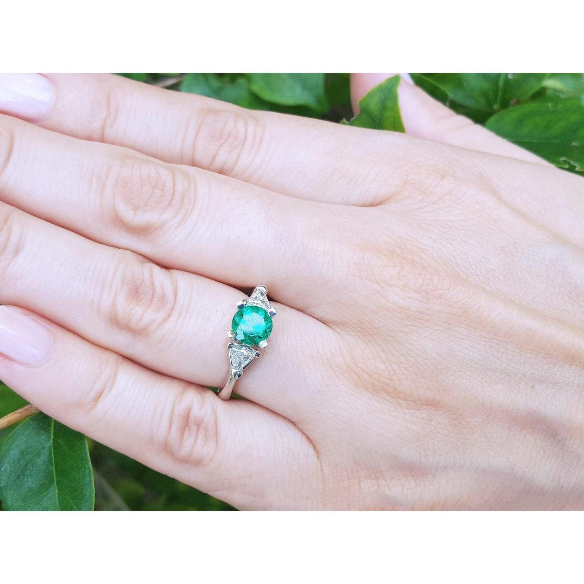 Hand wearing a women's three stone emerald ring against a green leafy background.
