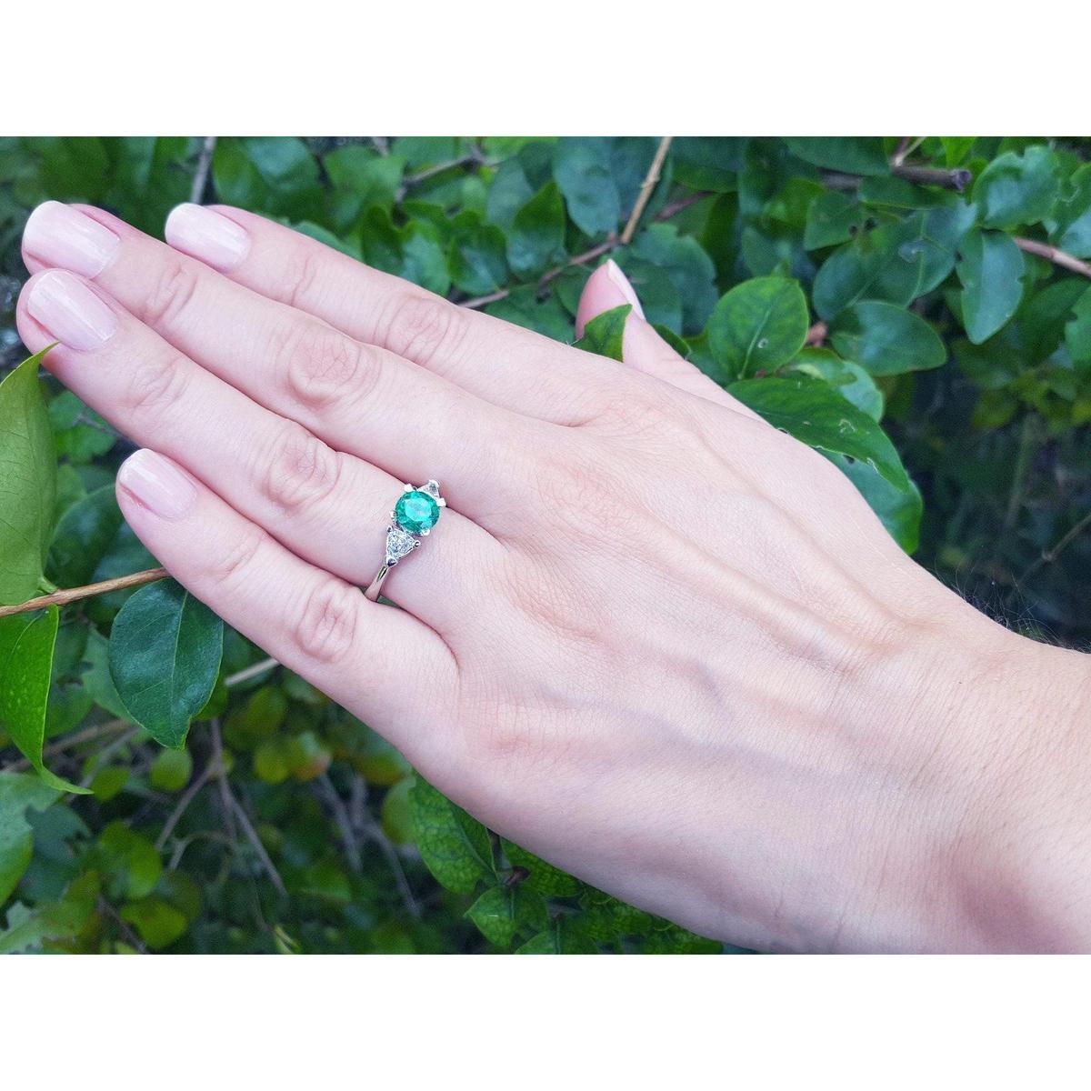 Hand wearing a three stone emerald ring for women with a green leafy background.