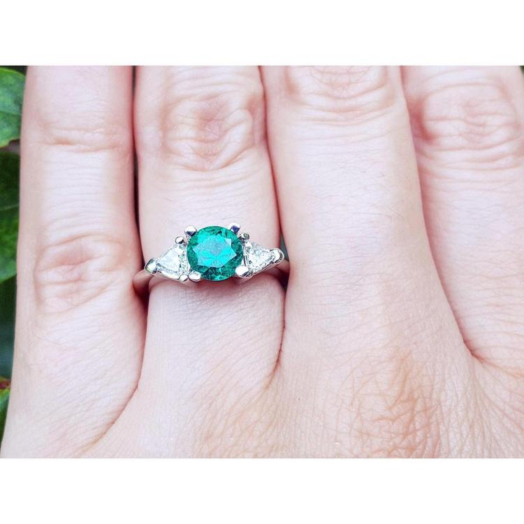 A lady's three stone natural colombian emerald ring round cut on a person's finger.