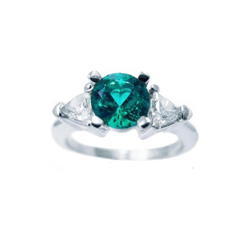 This round cut colombian emerald ring with trillion side diamonds is made of 14k white gold.