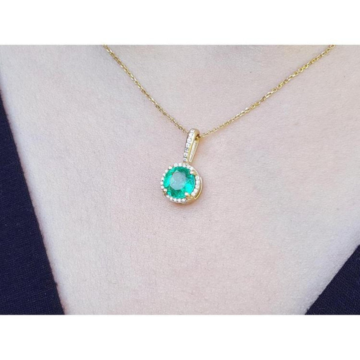 Round-cut natural emerald pendant necklace with halo diamonds on a 14K yellow gold chain.