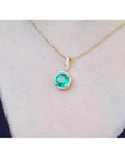 Round-cut natural emerald pendant necklace with halo diamonds on a 14K yellow gold chain.