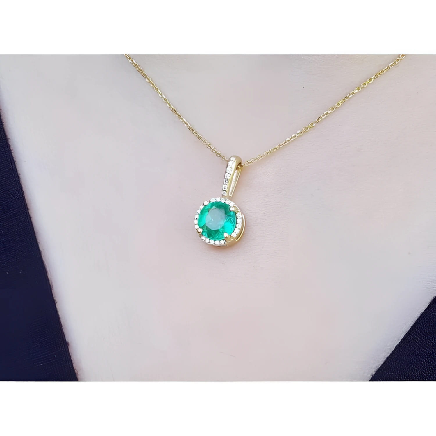 Round-cut natural emerald pendant necklace with halo diamonds on a 14K yellow gold chain.
