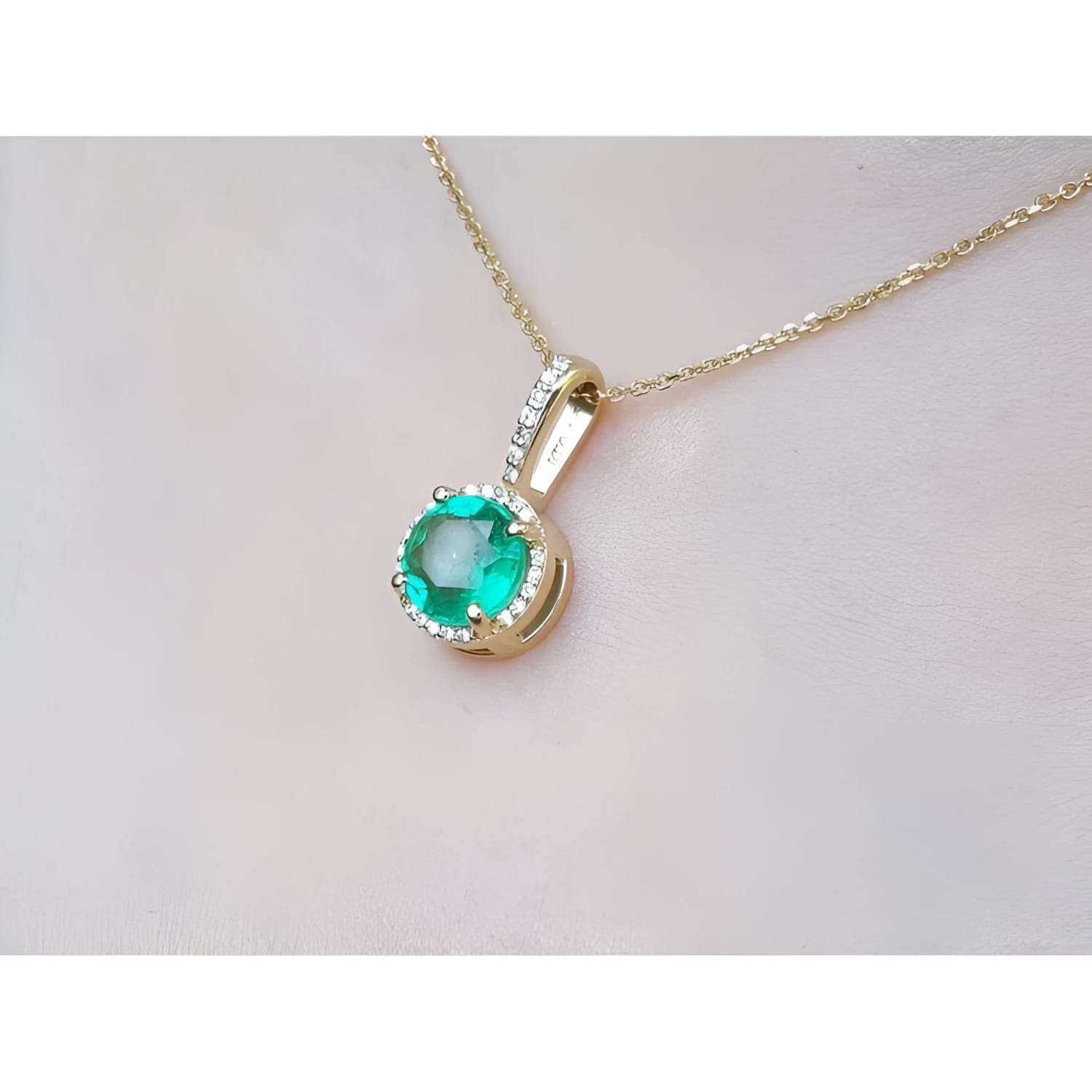 Gold necklace with a round cut natural colombian emerald pendant on a light pink skin background,