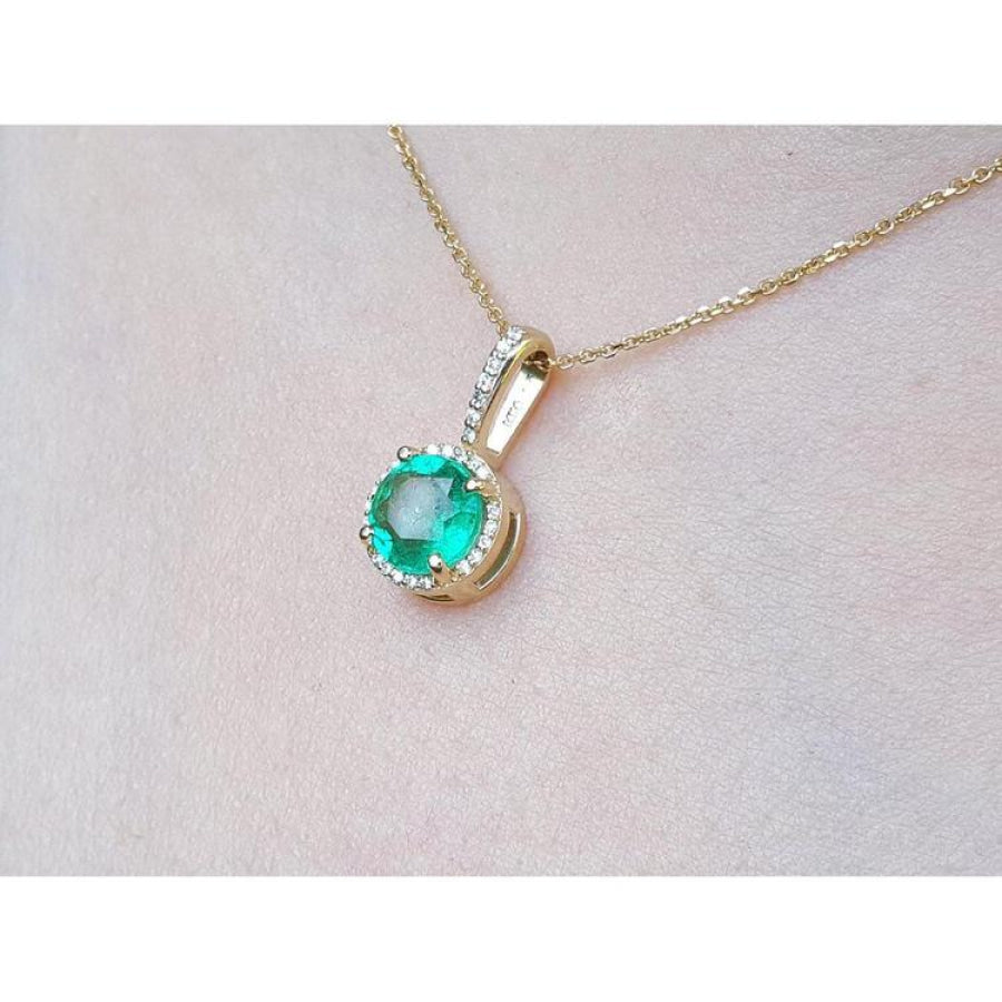 Gold necklace with a round cut natural colombian emerald pendant on a light pink skin background,