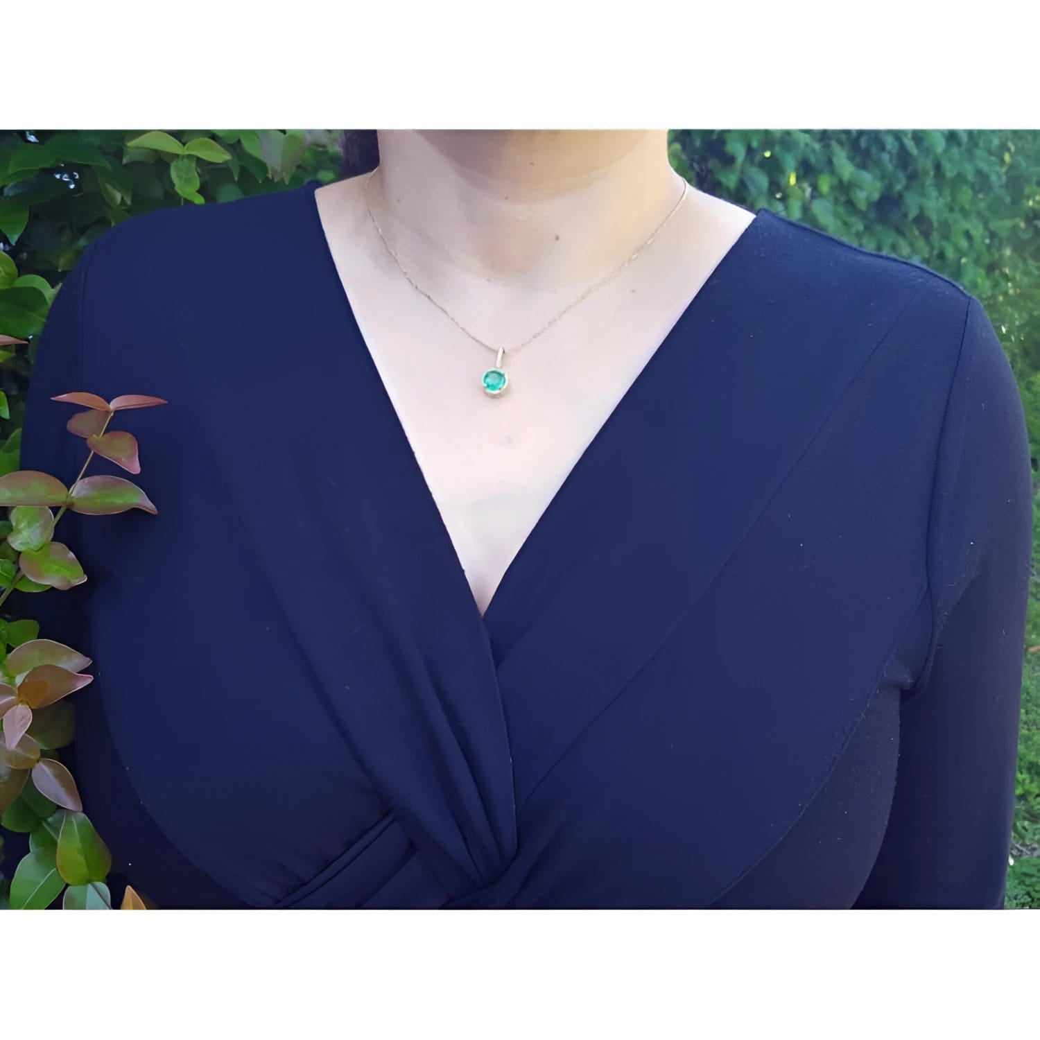 Woman wearing a 14K yellow gold pendant necklace with a round-cut green emerald and halo diamonds.