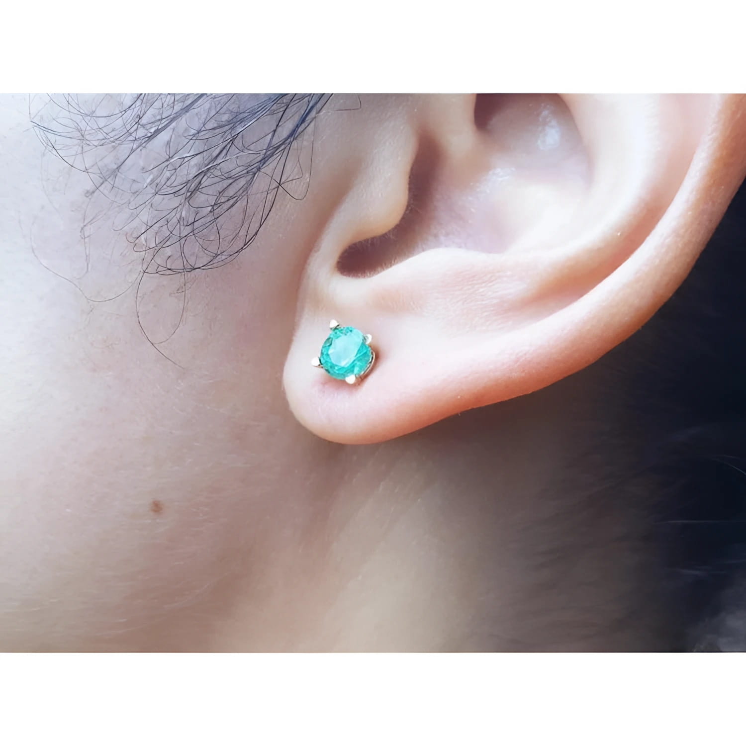 An earlobe wearing a round cut natural Colombian emerald stud earring in 14k gold.