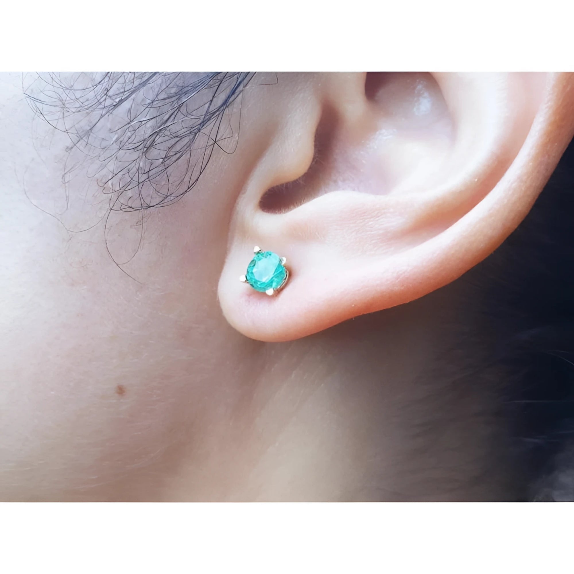 An earlobe wearing a round cut natural Colombian emerald stud earring in 14k gold.