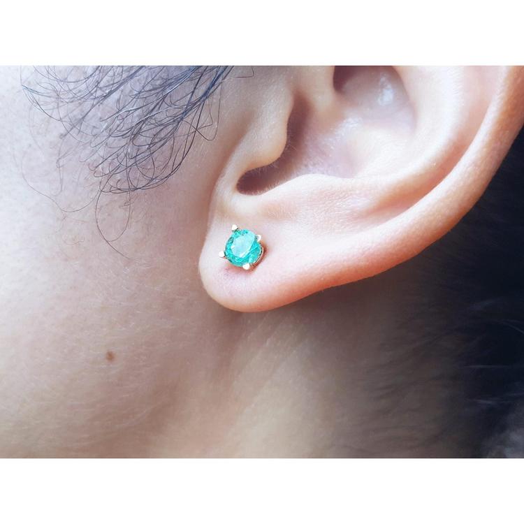 An earlobe wearing a round cut natural Colombian emerald stud earring in 14k gold.