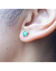 An earlobe wearing a round cut natural Colombian emerald stud earring in 14k gold.