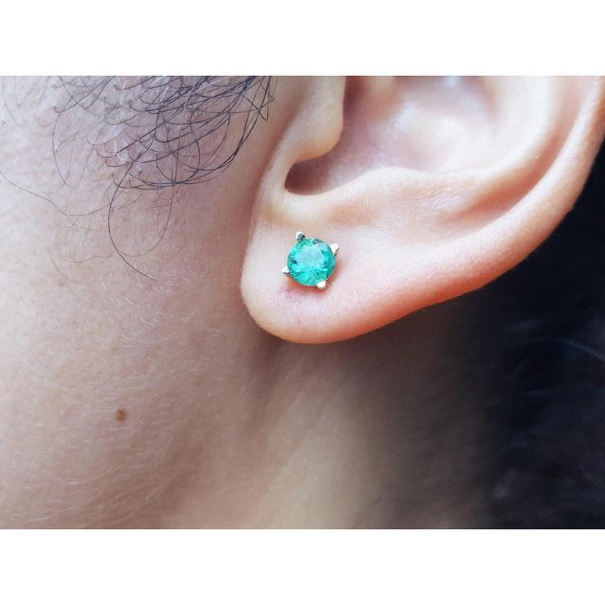 Round 1.09 ct. natural Colombian emerald stud earring in 14K gold basket setting on an ear.