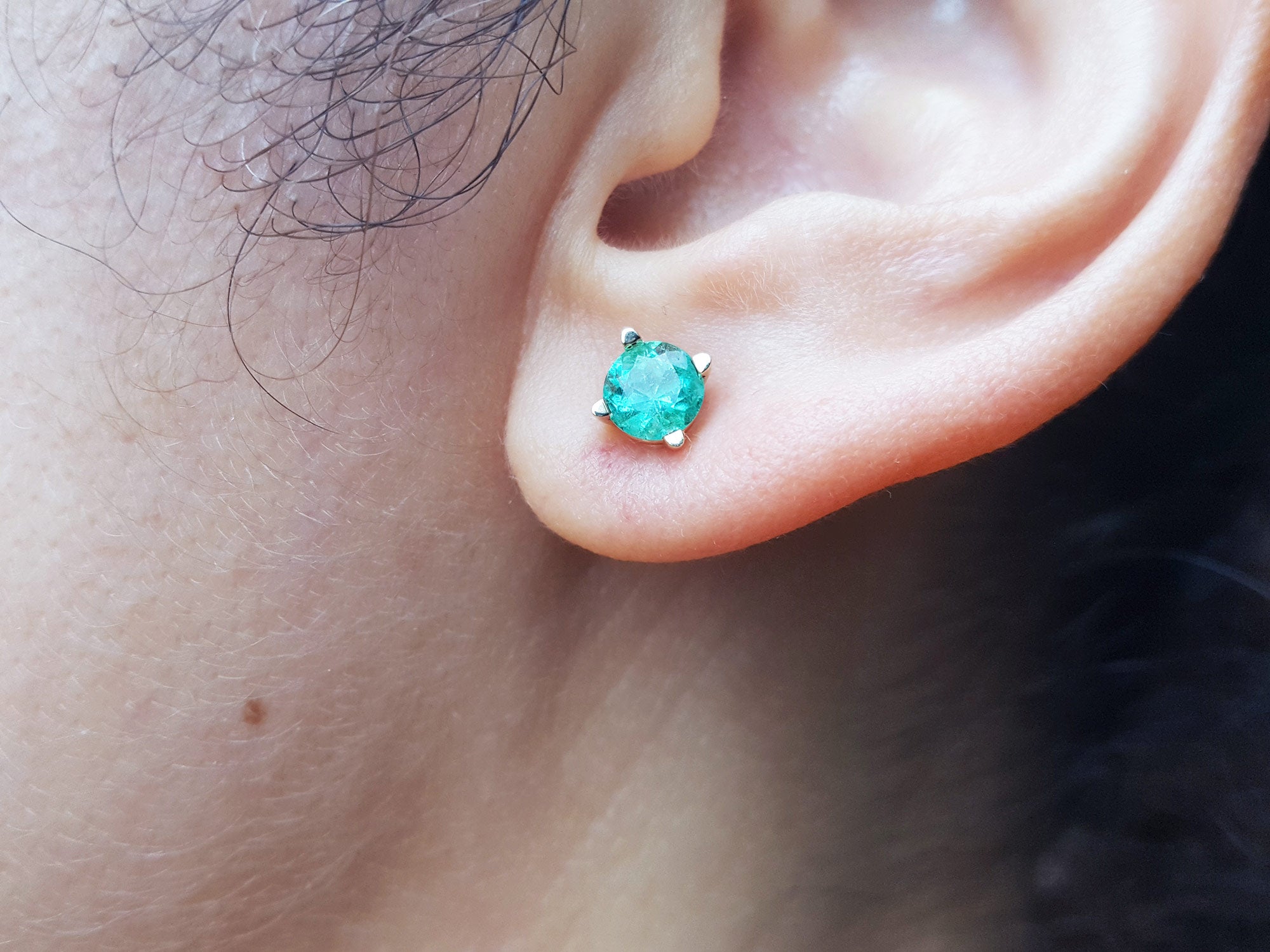 Close-up of an ear wearing a 14k yellow gold emerald stud round cut earring.